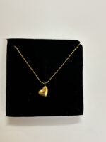 A gold plated heart necklace on a mannequin against a warm aesthetic background