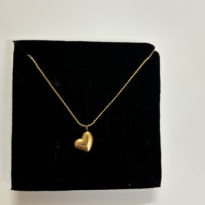 A gold plated heart necklace on a mannequin against a warm aesthetic background