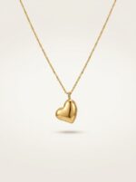 A close up of a gold plated heart necklace on black velvet display