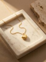 A close up of a gold plated heart necklace on black velvet display