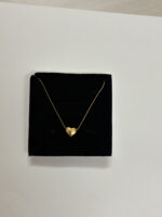 A close up of a gold plated heart necklace resting on rich emerald green silk
