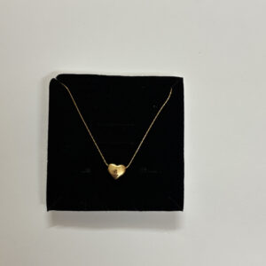 A close up of a gold plated heart necklace resting on rich emerald green silk