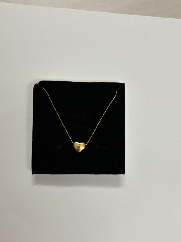 A close up of a gold plated heart necklace resting on rich emerald green silk