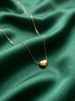Studio shot of a minimalist gold plated heart necklace against a cream background