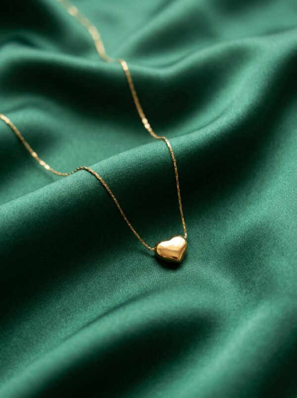 Studio shot of a minimalist gold plated heart necklace against a cream background