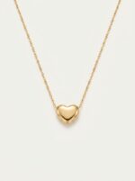 A delicate gold plated heart necklace on a black velvet display