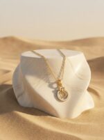 Close up of the gold plated necklace with a circular pendant on a black stand