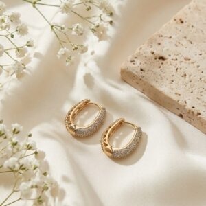 Close up of Aura pavé gold plated hoop earrings on textured cloth