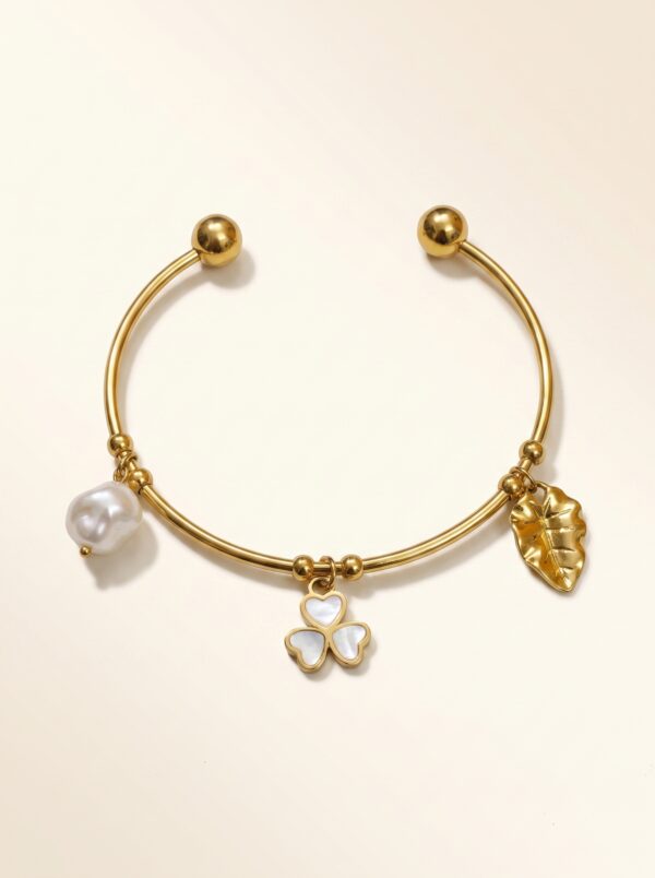 Close up of a gold plated kada featuring a clover floral charm and pearl
