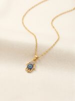 A Hamsa hand pendant necklace resting on a sculptural white stone against sand background