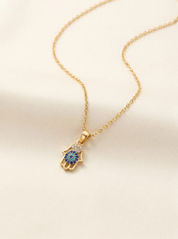 A Hamsa hand pendant necklace resting on a sculptural white stone against sand background