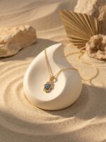 A delicate gold chain featuring a Hamsa hand pendant with blue and white stones