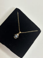A delicate gold chain featuring a Hamsa hand pendant with blue and white stones