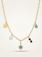 A gold plated necklace with various charms displayed on a black velvet stand