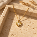 A delicate gold chain featuring a sculptural heart pendant with a glowing mother of pearl center